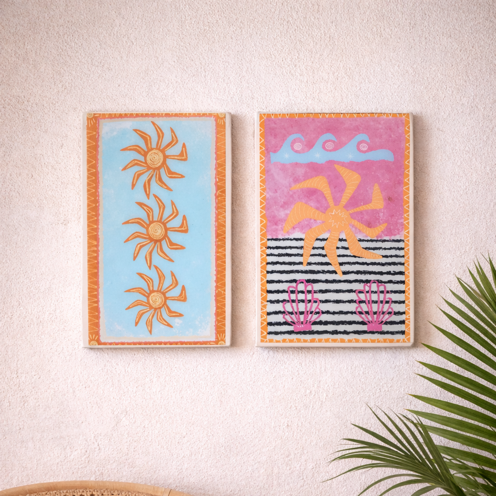 Two colorful abstract wall art pieces on a beige wall with a wicker chair and plant.