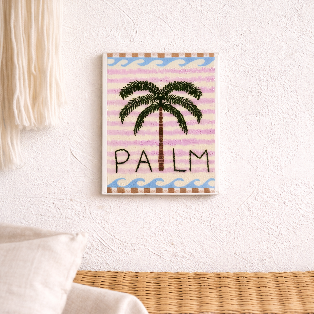 Framed artwork with palm tree design and 'Palm' text on a striped background, hanging on a wall.