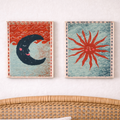 Two framed artworks of a crescent moon and a sun on a white wall above a wicker chair.